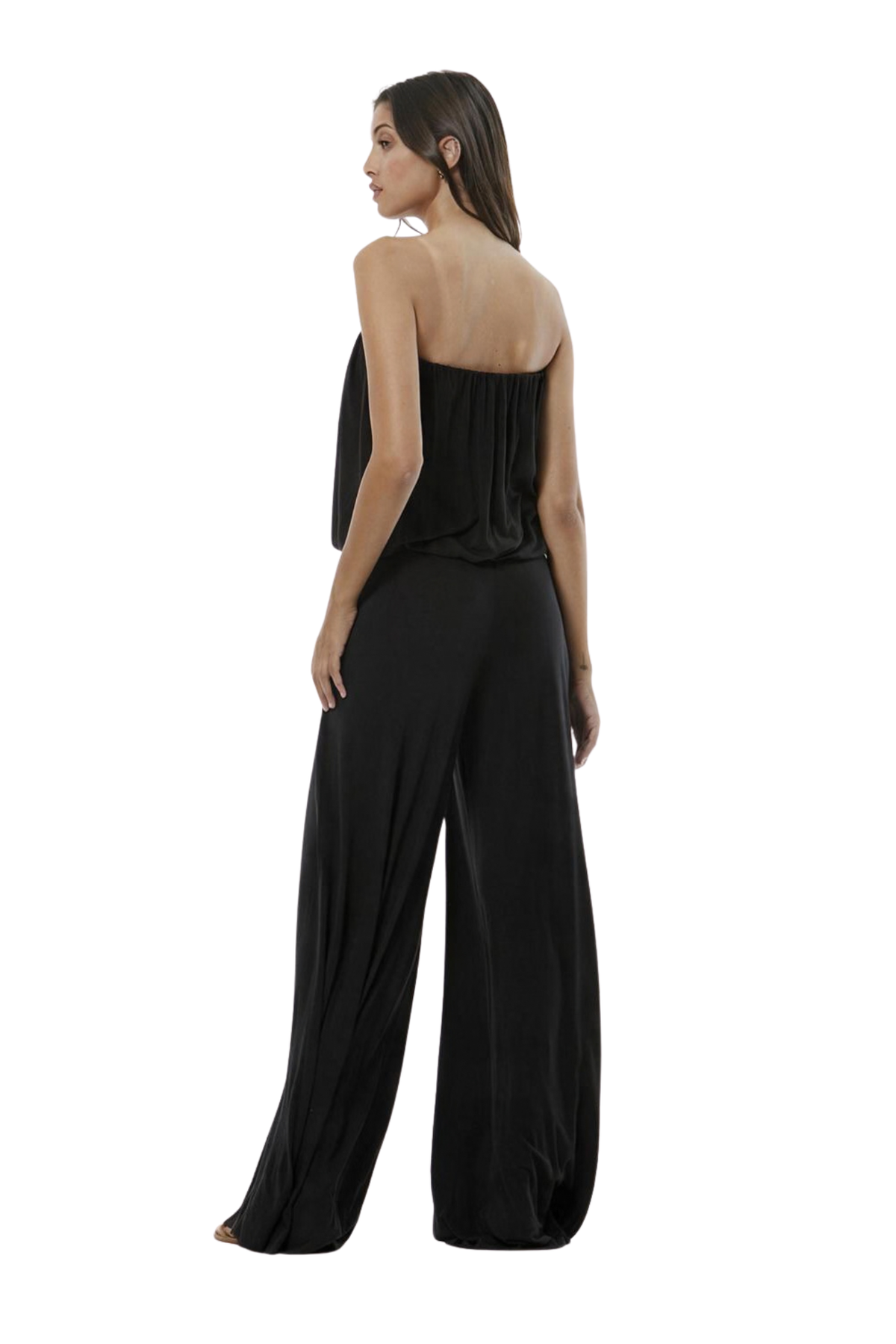 A woman modeling a black strapless jumpsuit with wide legs, photographed against a plain white studio background.