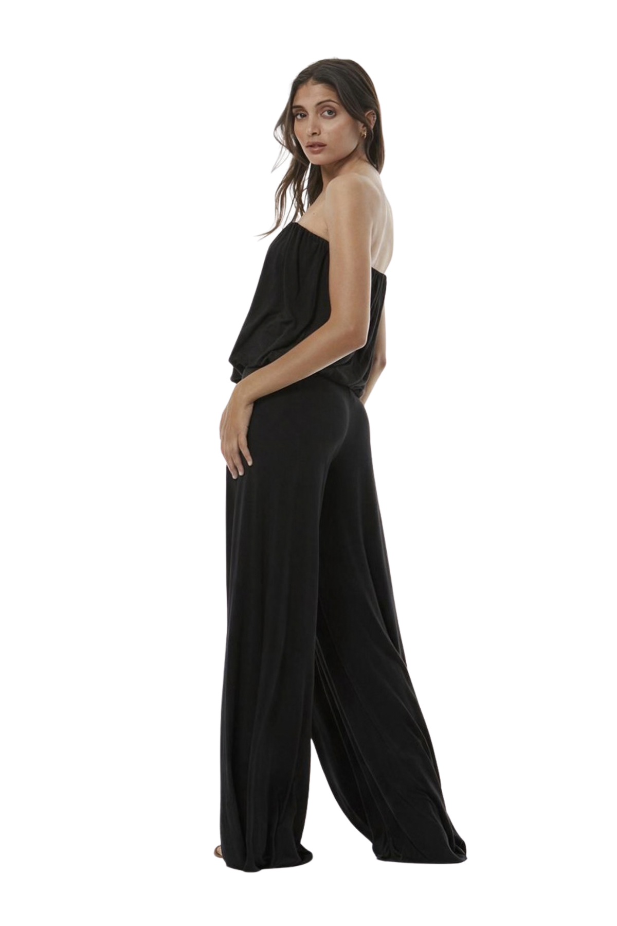 A woman modeling a black strapless draped jumpsuit with wide legs, shown from a side-back angle against a plain white background.