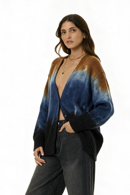 A woman modeling an open-front cardigan with a blue and brown tie-dye pattern and black ribbed trim, paired with dark gray pants against a plain white background.