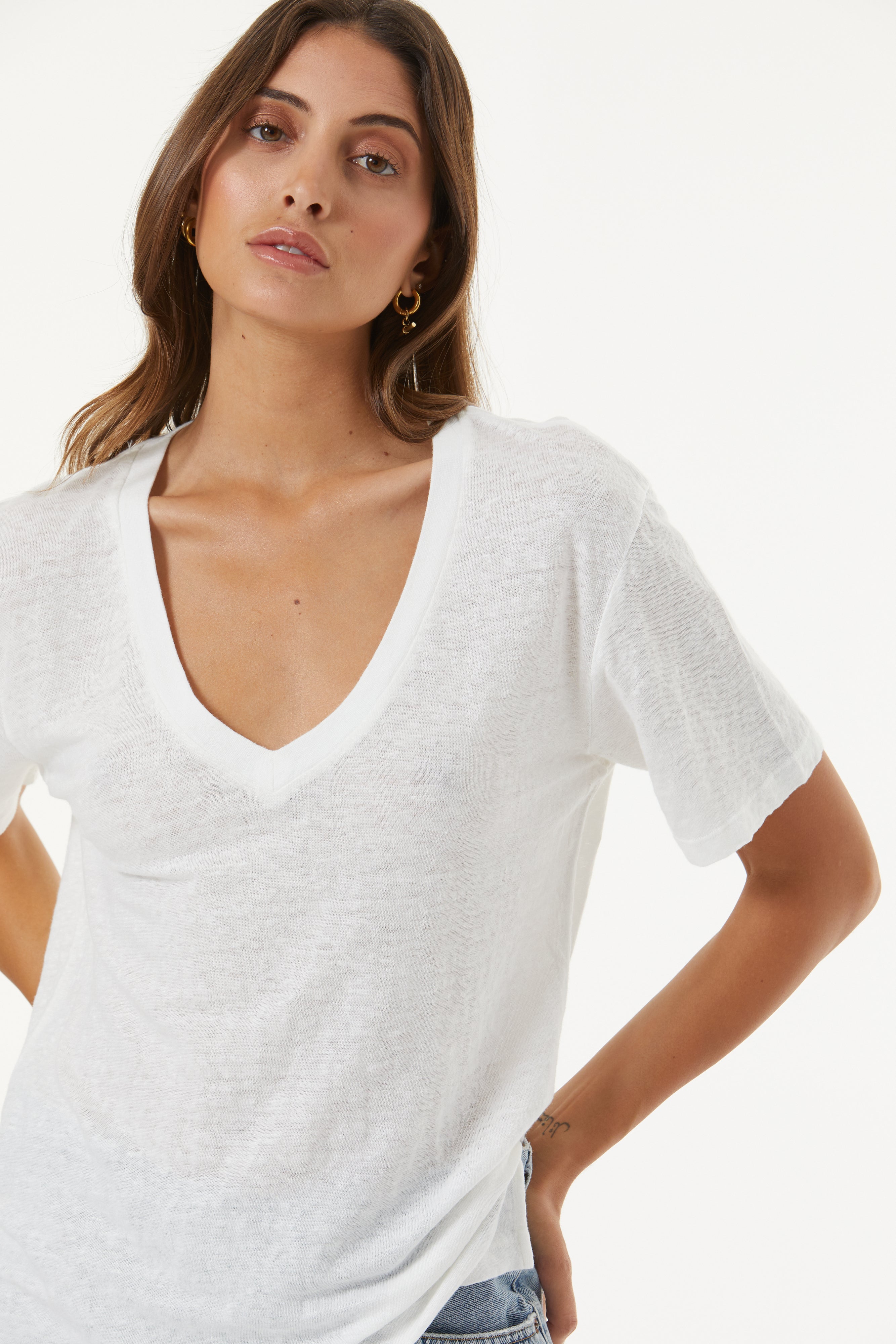 A woman wearing a white short-sleeve V-neck t-shirt, cropped from the chest down, against a plain white studio background.
