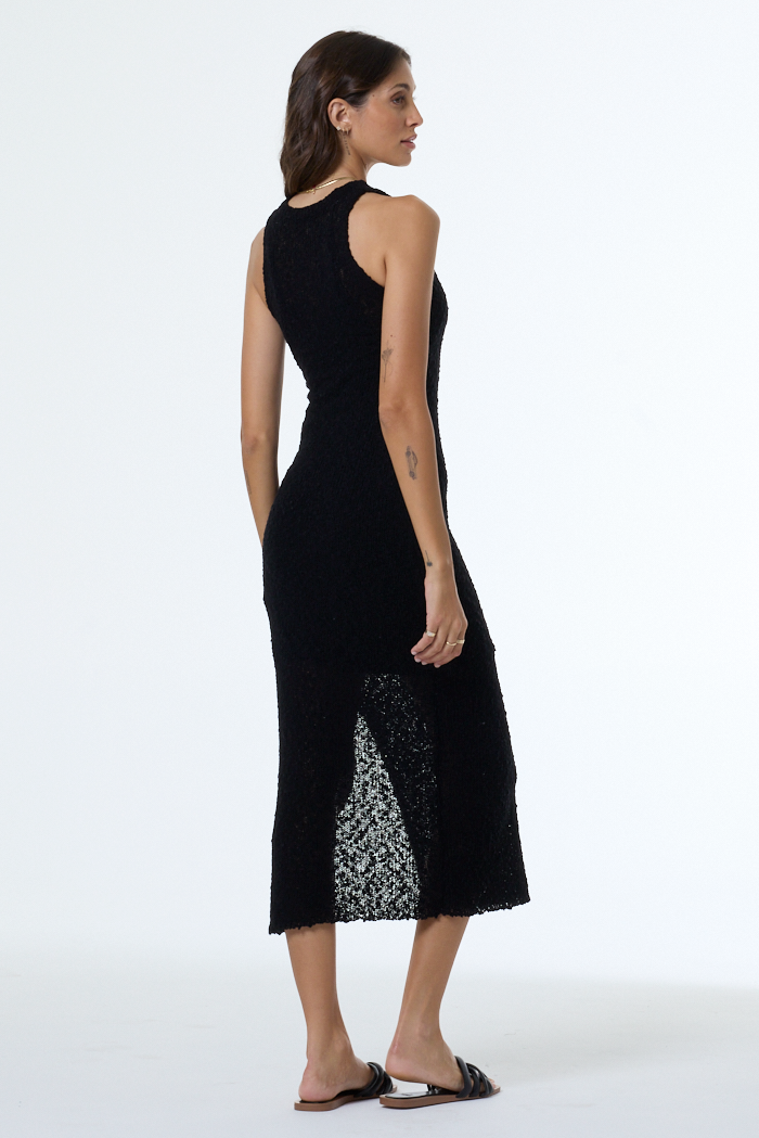 Woman wearing a black sleeveless dress with white lace detailing on a white background