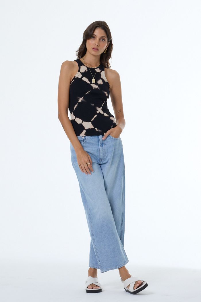 Woman wearing a black and white tie-dye sleeveless top and light blue jeans on a white background