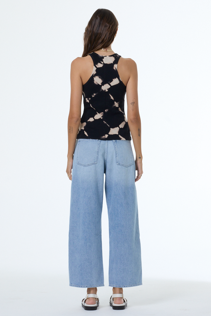Woman wearing a black and white patterned sleeveless top with light blue wide-leg pants on a white background