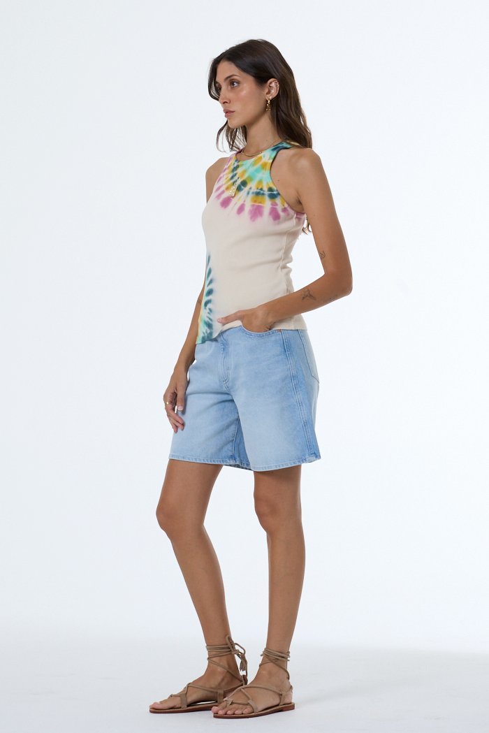 Woman wearing a tie-dye sleeveless top and light blue shorts on a white background