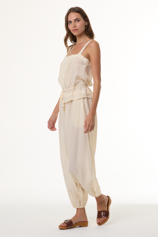 Woman wearing a beige sleeveless top and high-waisted pants on a white background