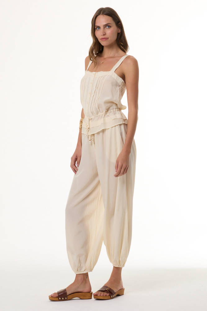 Woman wearing a cream-colored outfit with a top and harem pants on a white background