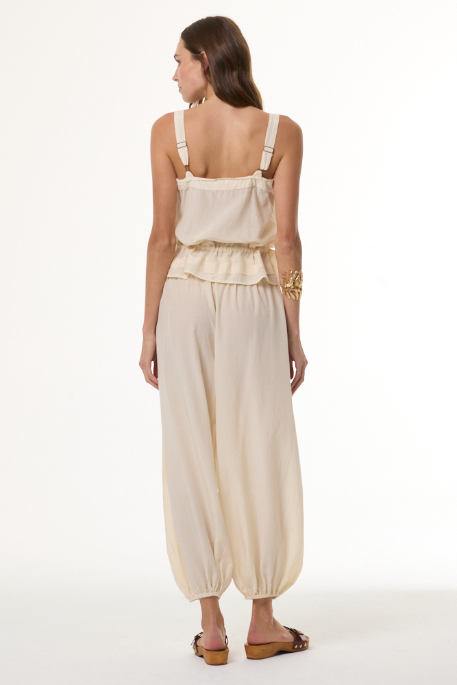 Woman wearing a beige sleeveless top and high-waisted pants on a white background