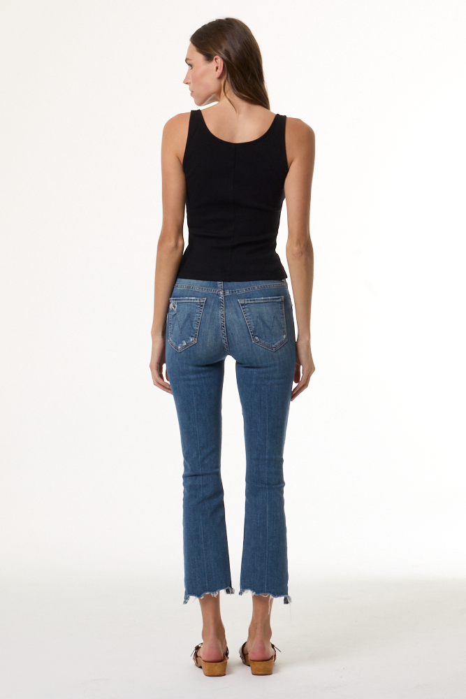 A woman shown from the back wearing a black sleeveless tank top, blue cropped flare jeans with a raw hem, and brown wedge sandals against a plain white studio background.