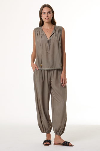 Woman wearing a sage sleeveless top and harem pants on a white background