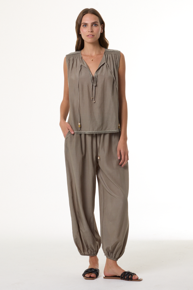 Woman wearing a sage sleeveless top and harem pants on a white background