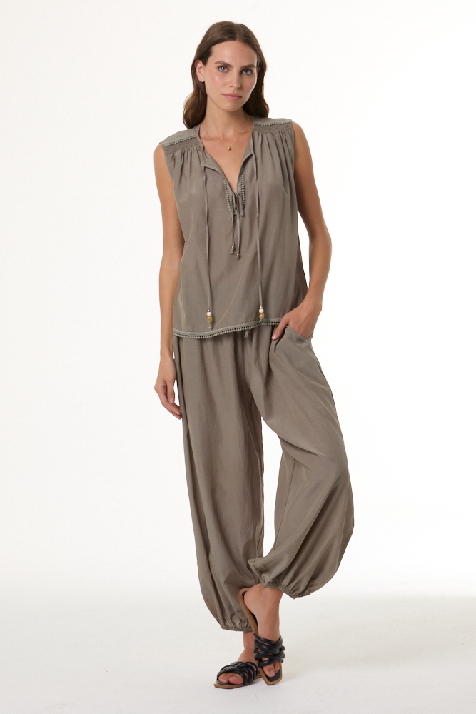 Woman wearing a sage sleeveless top and harem pants on a white background