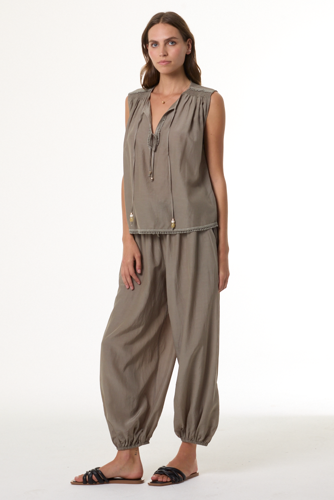 Woman wearing a sage sleeveless top and harem pants on a white background