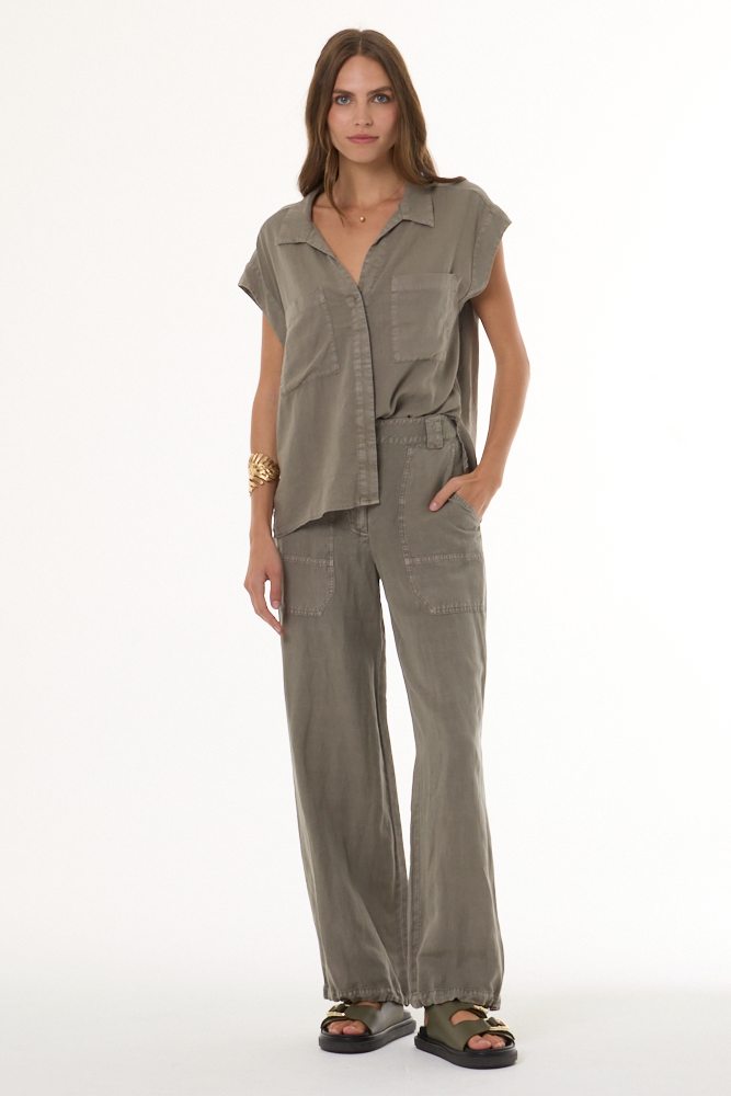 A woman modeling a matching two-piece set consisting of a short-sleeve button-front shirt and wide-leg pants in a muted taupe-gray color, styled with black sandals against a plain white studio background.