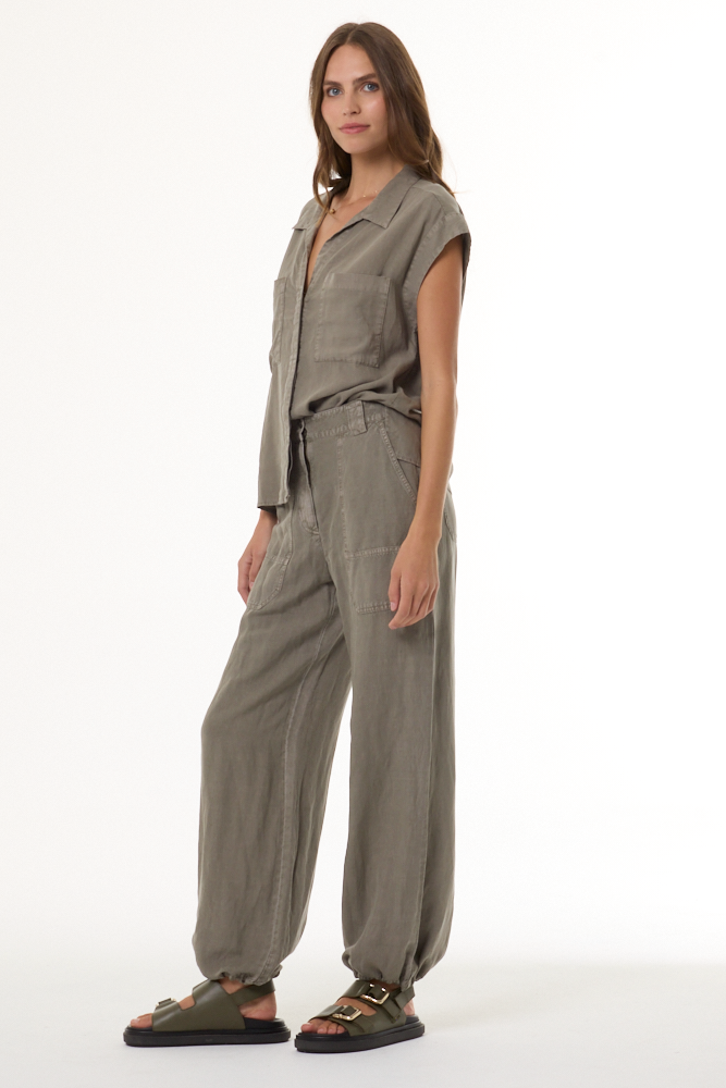 A woman modeling a taupe-gray sleeveless button-up shirt and matching wide-leg pants set, paired with dark brown slide sandals, against a plain white studio background.