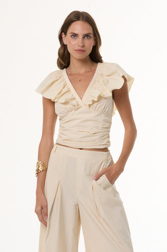 A woman modeling a cream-colored ruffled wrap top with short flutter sleeves and matching high-waisted wide-leg trousers against a plain white studio background.