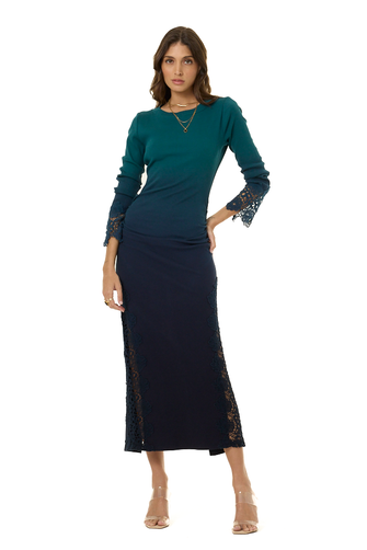 A woman modeling a long-sleeve midi dress with a dark teal top fading into a dark navy skirt, featuring lace detailing on the cuffs and sides, set against a plain white background.