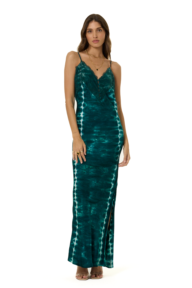 A woman modeling a long, sleeveless maxi dress with a tie-dye pattern in deep teal green and white, set against a plain white background.