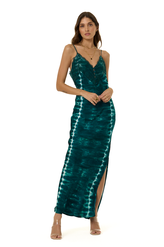 A woman modeling a long teal tie-dye maxi dress with spaghetti straps, a V-neckline, and a high side slit, photographed against a plain white background.