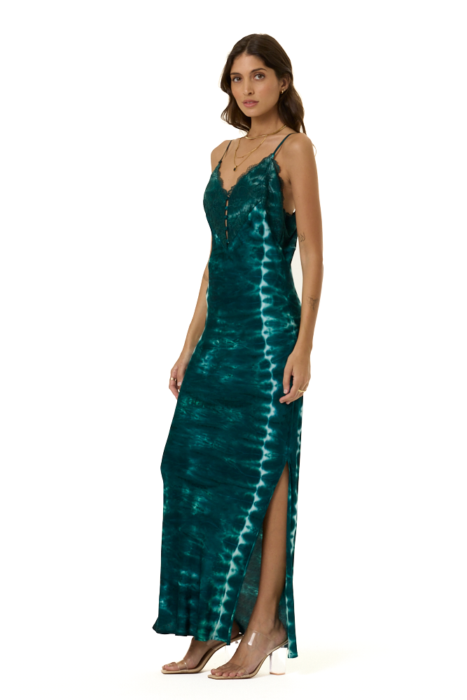 A woman modeling a sleeveless, floor-length teal tie-dye maxi dress with spaghetti straps, a V-neckline, and a high side slit, photographed against a plain white background.