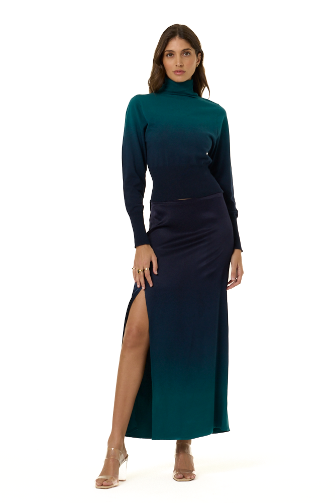 A woman modeling a long-sleeve turtleneck top with a dark teal-to-navy ombre gradient, paired with a matching dark navy to teal ombre skirt, against a plain white background.