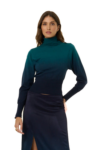 A woman modeling a long-sleeve turtleneck top with a dark teal-to-navy ombre gradient, paired with a matching dark navy to teal ombre skirt, against a plain white background.