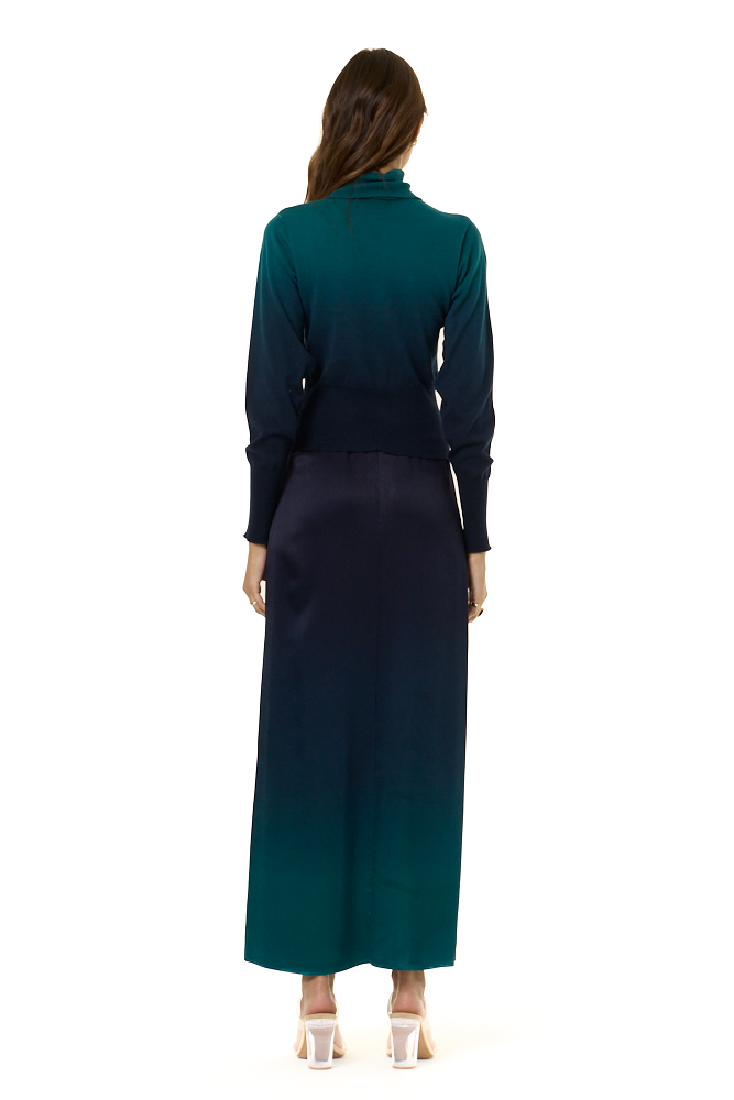 A woman view from the backside modeling a long-sleeve turtleneck top with a dark teal-to-navy ombre gradient, paired with a matching dark navy to teal ombre skirt, against a plain white background.