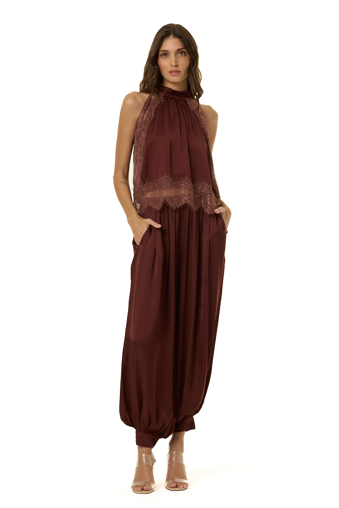 A woman modeling a sleeveless high-neck outfit in deep burgundy brown, featuring a sheer lace halter top and voluminous gathered harem-style pants, photographed against a plain white background.