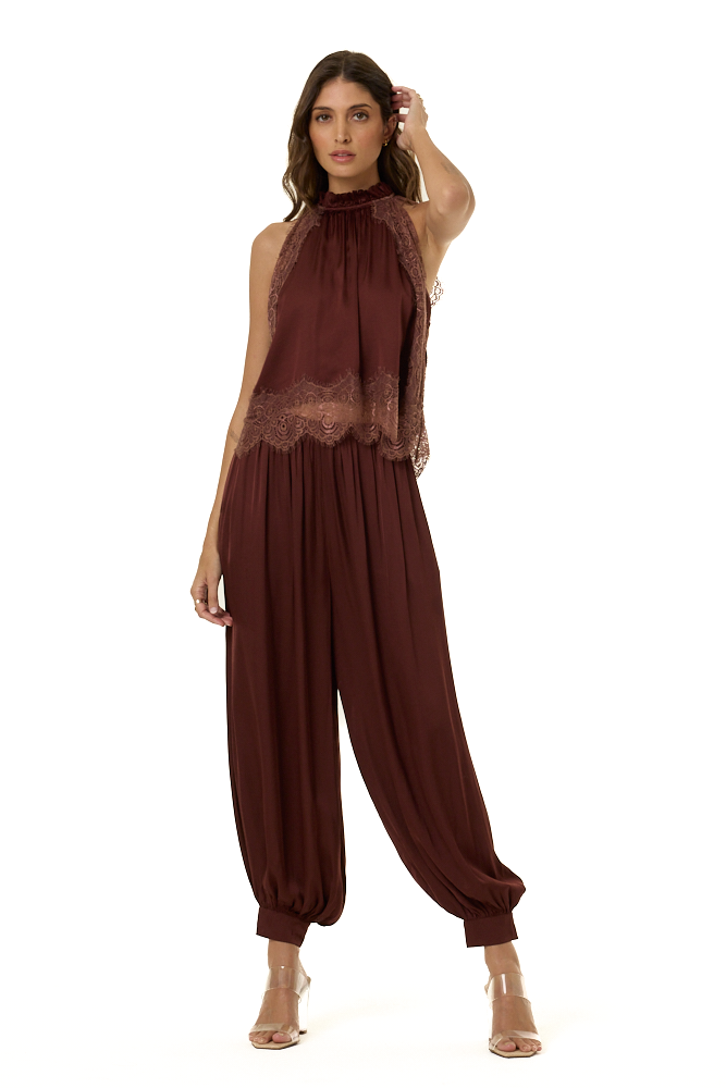 A woman modeling a sleeveless high-neck top in deep burgundy and lace trim at the bust and waist with matching harem pants, shown against a plain white background.