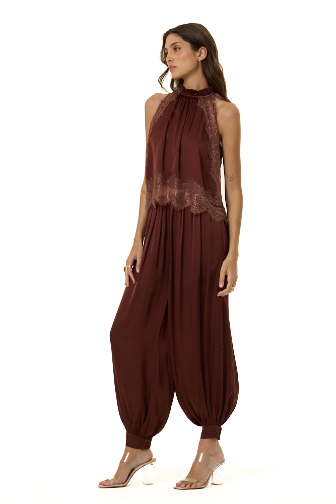 A woman modeling a sleeveless high-neck top in deep burgundy and lace trim at the bust and waist with matching harem pants, shown against a plain white background.