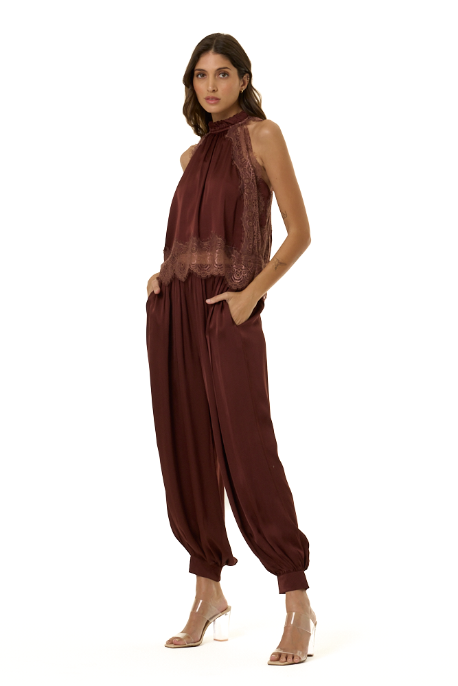 A woman modeling a sleeveless high-neck outfit in deep burgundy brown, featuring a sheer lace halter top and voluminous gathered harem-style pants, photographed against a plain white background.