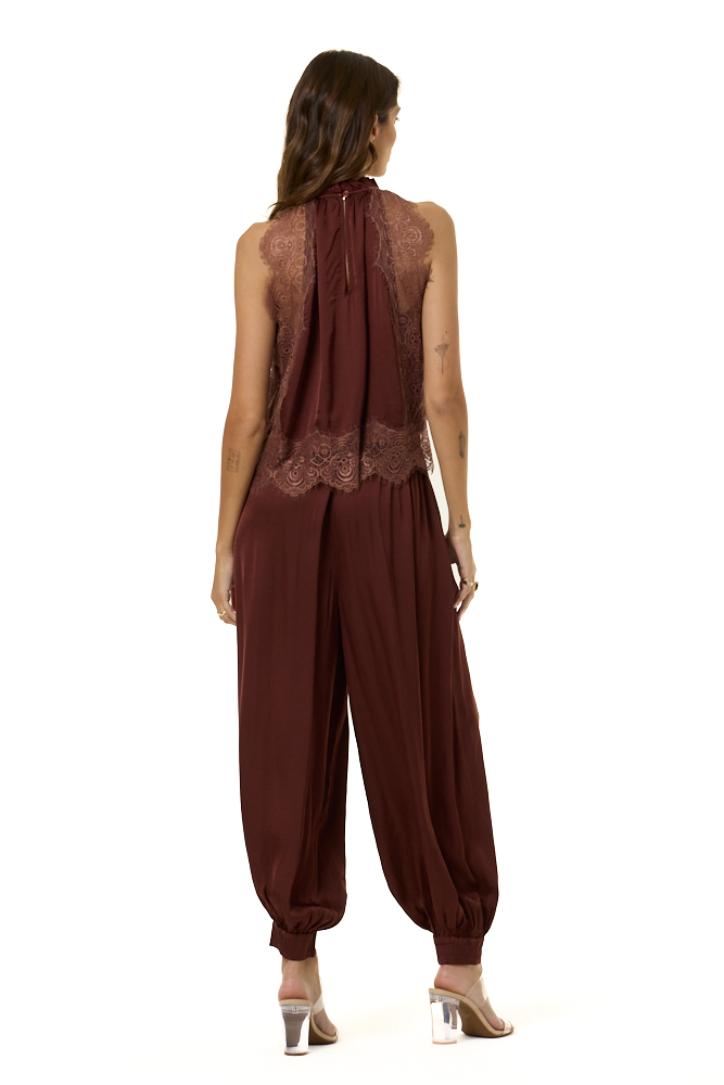 A woman viewed from the back wearing a sleeveless harem-style outfit in deep burgundy with sheer lace panels at the upper back, photographed against a plain white studio background.