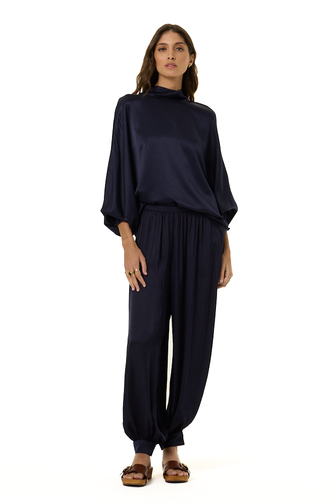 A woman modeling a dark navy blue two-piece outfit consisting of a loose, high-neck long-sleeve top and matching wide-leg pants, paired with brown sandals, against a plain white background.