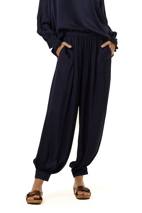 A person wearing loose navy blue harem-style pants with side pockets, paired with a matching top and brown sandals, shown against a plain white background.
