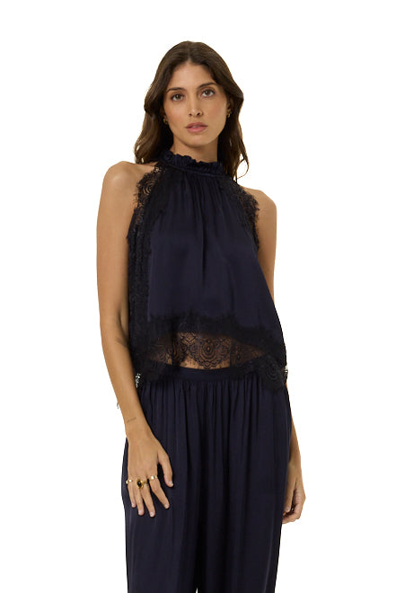 A woman modeling a sleeveless navy blue top with lace trim and a smocked neckline, paired with matching navy harem pants, against a plain white background.