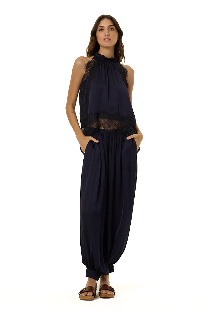 A woman modeling a sleeveless navy blue top with lace trim and a smocked neckline, paired with matching navy harem pants, against a plain white background.