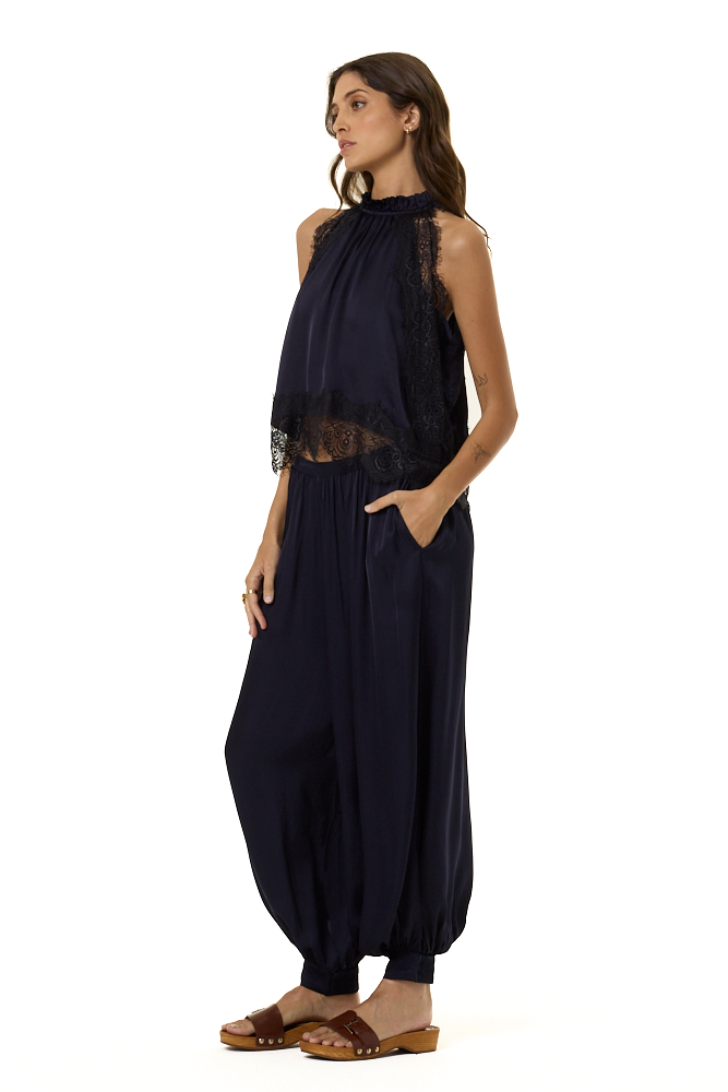 A woman modeling a sleeveless navy blue top with lace trim and a smocked neckline, paired with matching navy harem pants, against a plain white background.