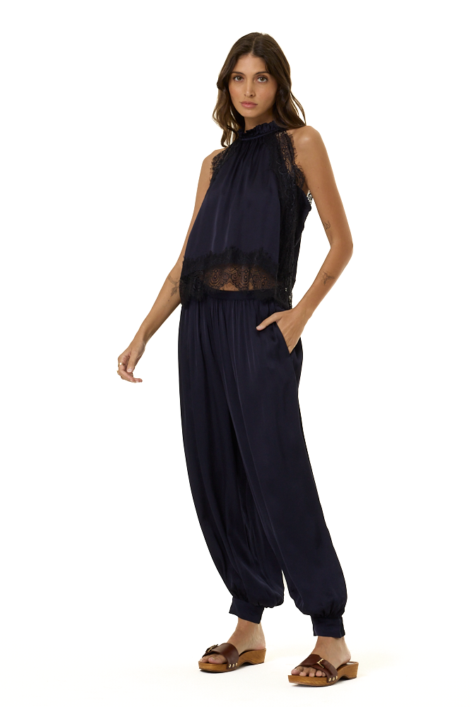 A woman modeling a sleeveless navy blue halter top with ace trim and matching navy harem-style pants, paired with brown sandals, against a plain white background.