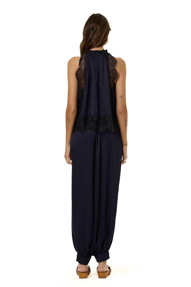 A woman viewed from the backside wearing a sleeveless navy blue top with lace trim and a smocked neckline, paired with matching navy harem pants, against a plain white background.