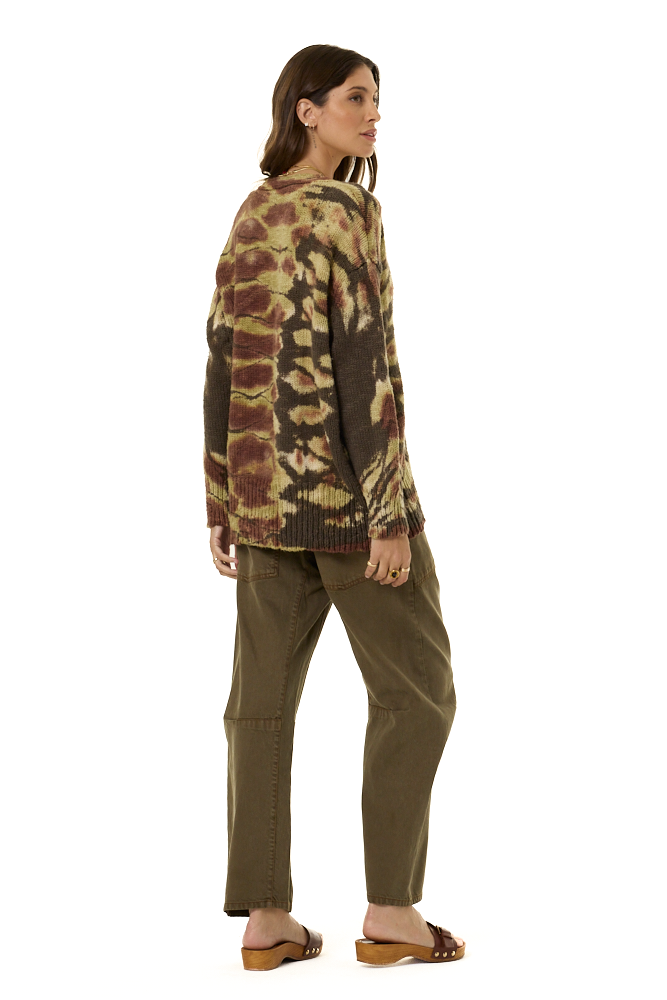 A woman shown from the back wearing a long-sleeve knit sweater with a brown, beige, and olive tie-dye pattern, paired with olive green pants and brown slide sandals, against a plain white background.