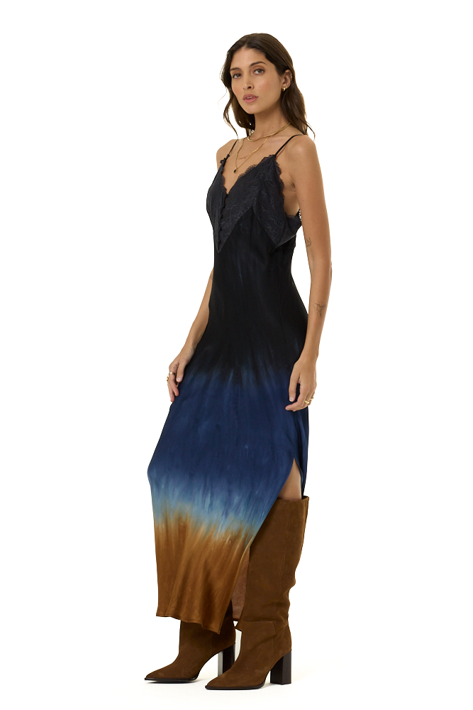 A woman modeling a sleeveless maxi dress with a black-to-blue gradient upper body and a blue-to-brown gradient lower skirt, paired with brown knee-high boots, against a plain white background.