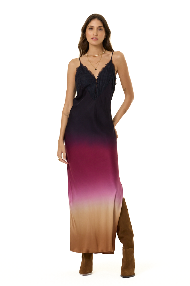 A woman modeling a sleeveless maxi dress with a gradient ombre design transitioning from black at the top to magenta and tan at the bottom, paired with brown suede boots, on a solid white background.