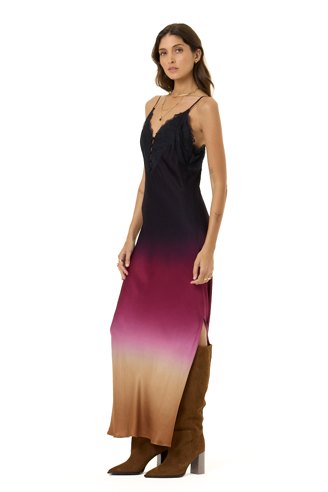A woman modeling a sleeveless maxi dress with a black-to-purple-to-cream ombré gradient, paired with brown knee-high boots, against a plain white background.