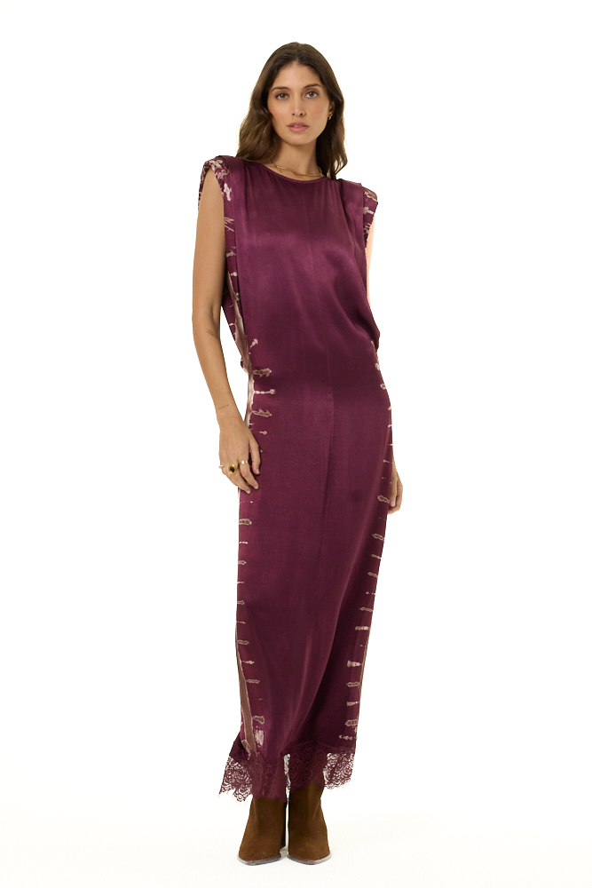 A woman modeling a sleeveless, floor-length mauve satin dress with lace trim , paired with brown suede boots, against a plain white background.