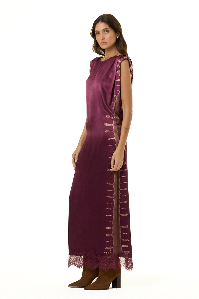 A woman modeling a sleeveless, floor-length plum purple dress with lace trim, paired with brown boots, against a plain white background.