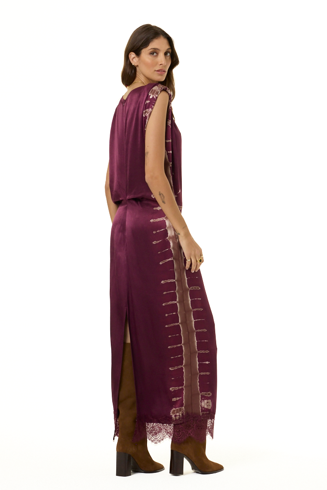 A woman modeling a long, sleeveless plum-purple maxi dress with lace trim and brown ankle boots, shown from a side-back angle against a plain white background.