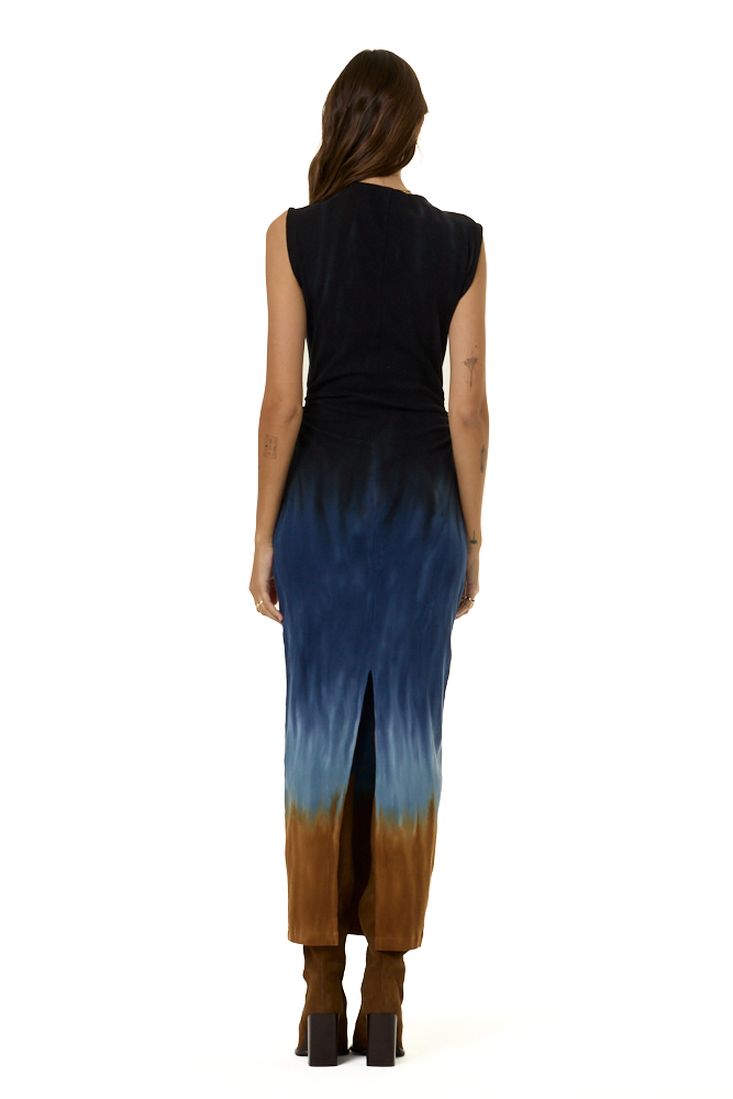 A woman viewed from the back wearing a sleeveless maxi dress with a gradient design that transitions from black at the top, through deep blue in the middle, to brown at the bottom, paired with brown heeled boots against a white background.
