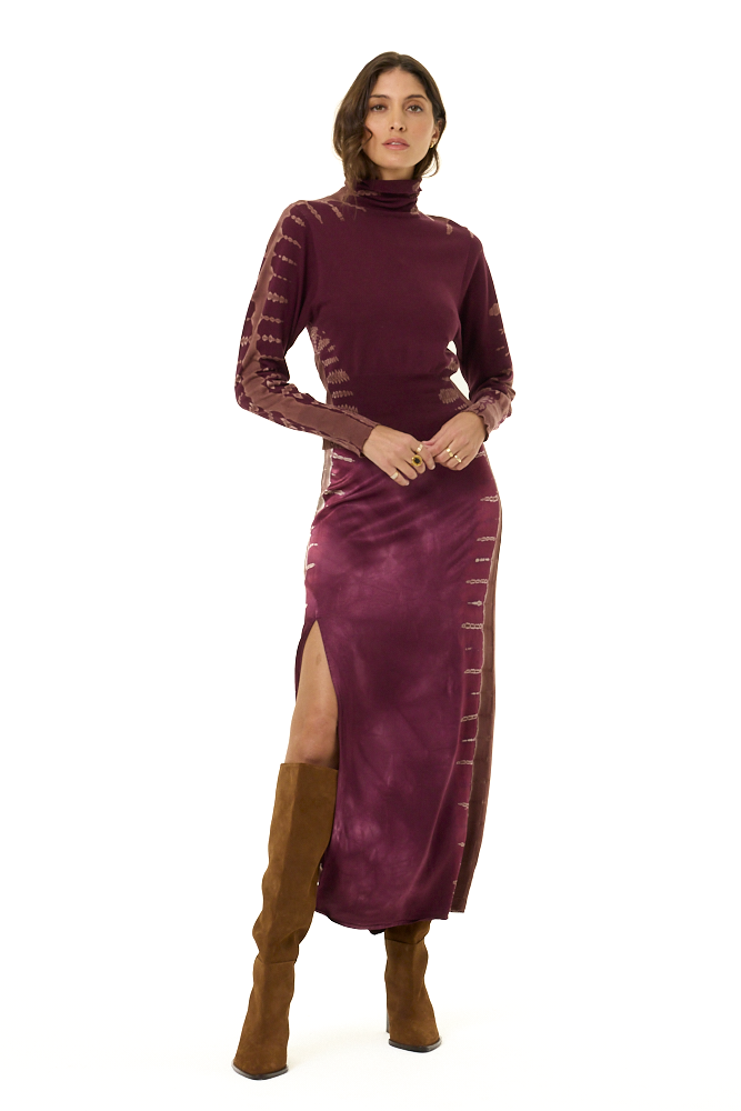 A woman modeling a long-sleeve turtleneck dress in deep plum purple, featuring textured knit sleeves and a satin-like skirt, set against a plain white background.