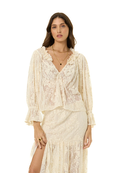 A woman modeling a cream lace two-piece set consisting of a long-sleeve tie-front top and a matching high-slit skirt, photographed against a plain white background.