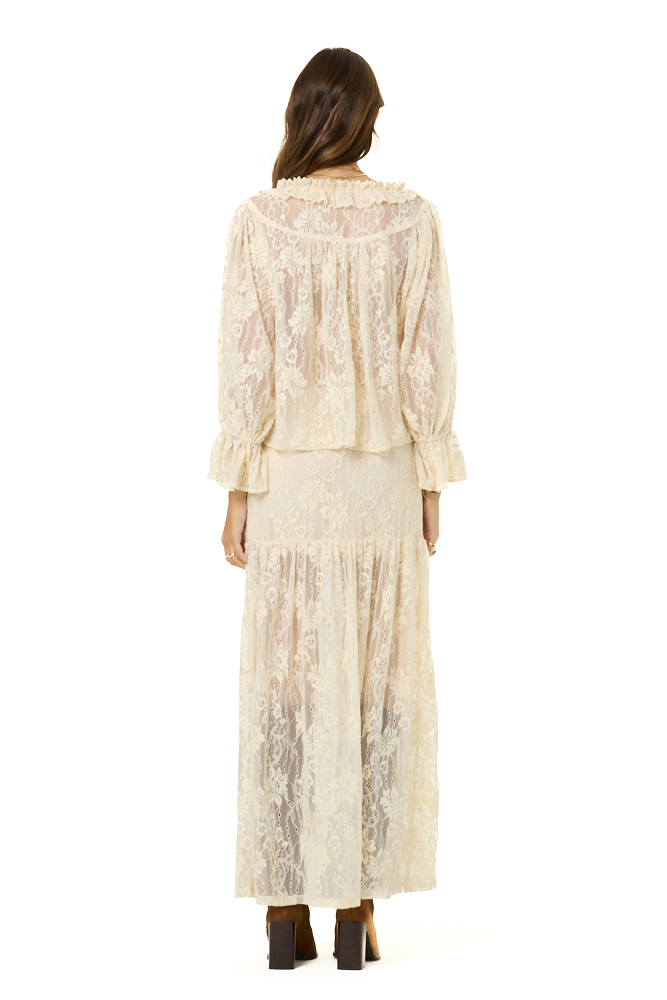 A woman viewed from the back wearing a cream lace long-sleeve top and matching maxi skirt against a plain white background.