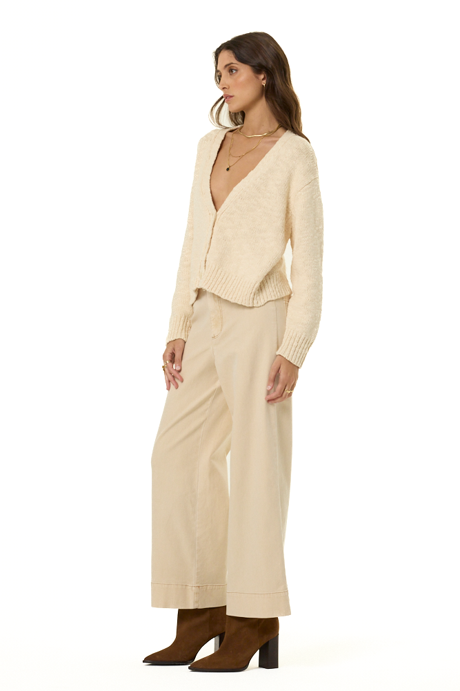 A woman modeling a cream-colored knit cardigan and matching wide-leg trousers, paired with brown ankle boots, against a plain white background.